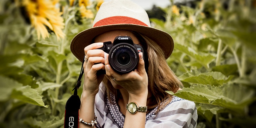 A picture of a girl with a brown hat holding a DSLR camera and clicking pictures.