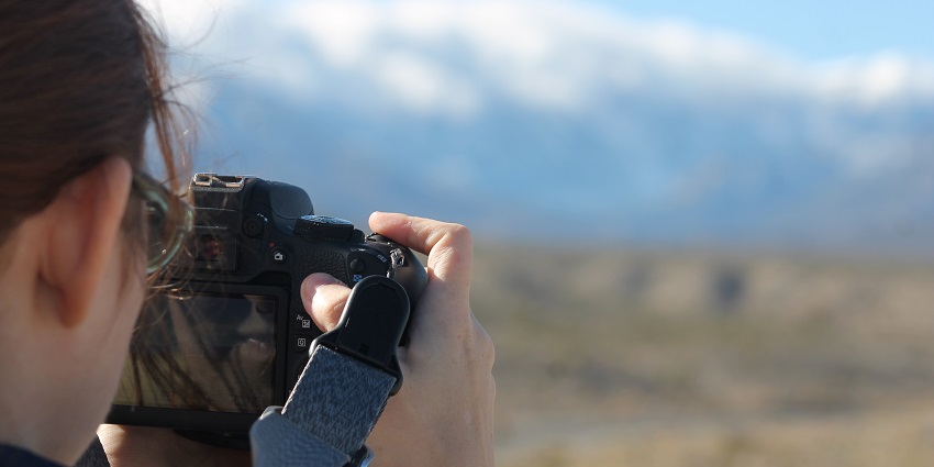 A picture of a girl clicking a picture of snow-covered mountains with a DSLR camera.