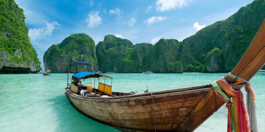 A picture of a ferry in the crystal clear waters of Phuket with the green hill-like island in the background