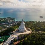 An image of a light sky and blue ocean behind the big Buddha Statue in Phuket, Thailand.