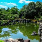 A scenic view of a park covered with verdant grasses, lush green trees, and flowers.