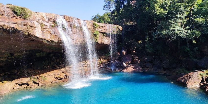 Witness the turquoise pool of this fall nestled in a quaint cave amidst lush wilderness