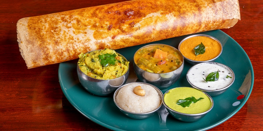 A golden-brown dosa served on a plate, accompanied by chutney and sambar for dipping.