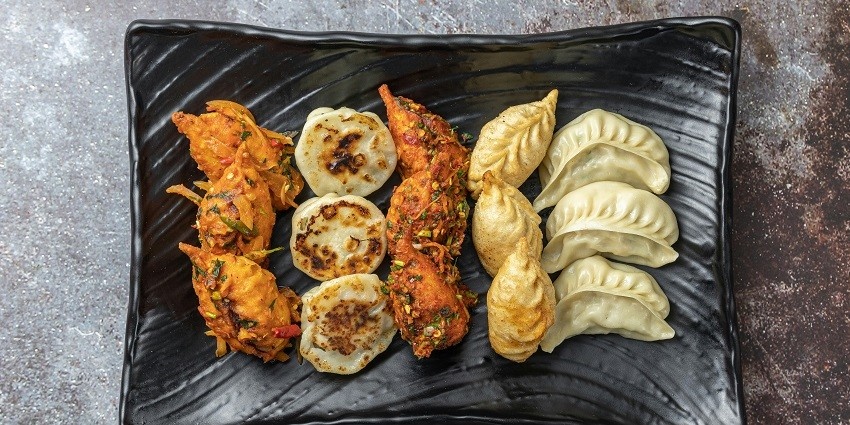Freshly steamed momo on a black tray, showcasing its rustic texture and warm colour.