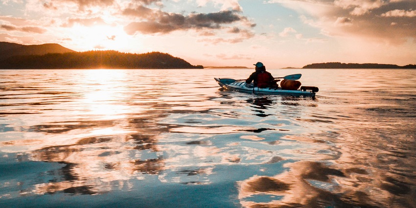 Person sitting on a teal kayak on calm river water, reflecting a tranquil kayaking.
