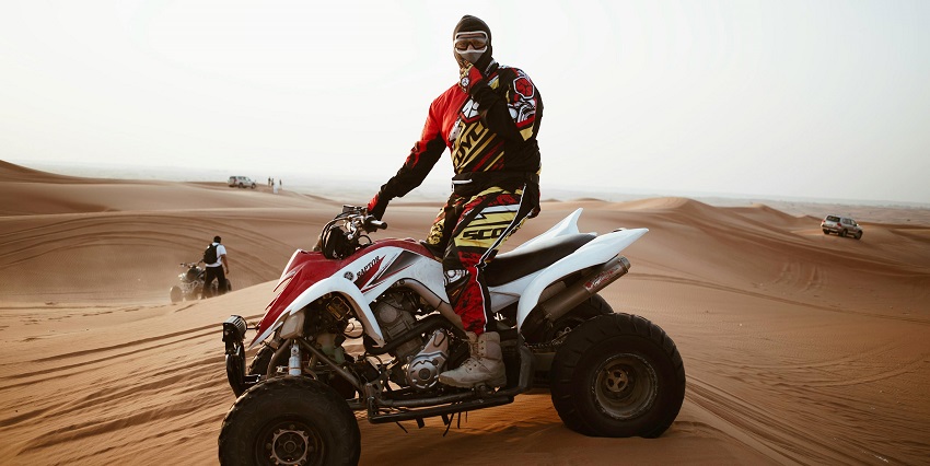 A picture of a man riding a quad bike in desert sand with his face covered
