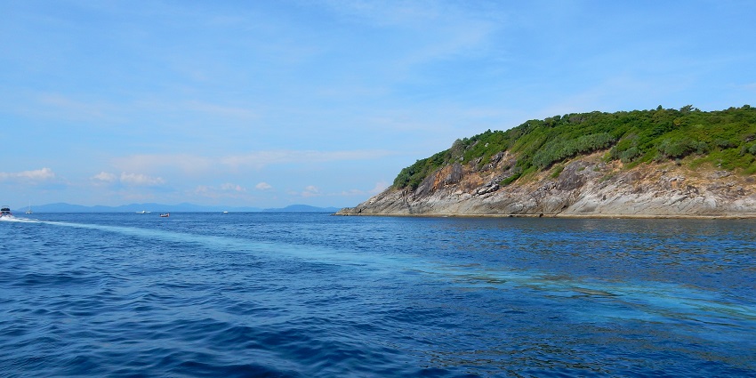 A picture of an island taken from a beach with clear blue waters nearby