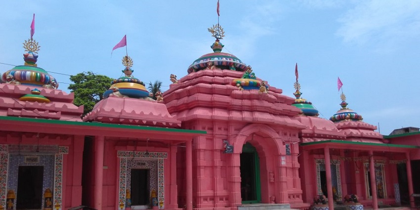 A picture of a red-walled temple in Kullu with Hindu architecture and flags on the roof