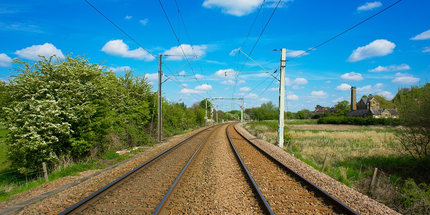 Railway tracks stretching into the distance, flanked by green fields and a clear sky.