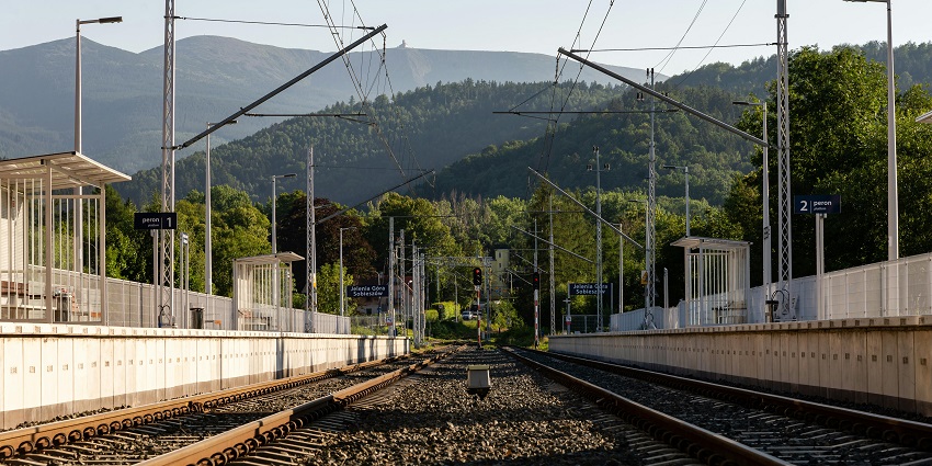 Picturesque view of train rail near lush greenery mountains and clear blue sky.