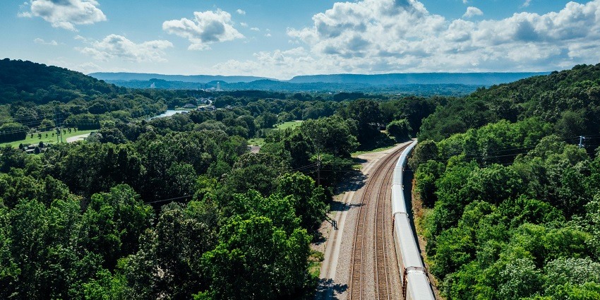 Railway tracks cutting through a dense forest, surrounded by trees and vibrant foliage.