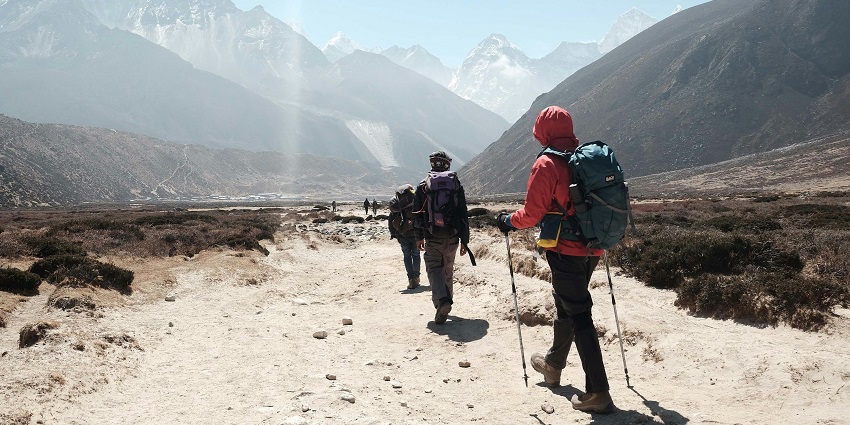 A picture of people on a rocky and sandy terrain with a backdrop of snow-clad peaks.