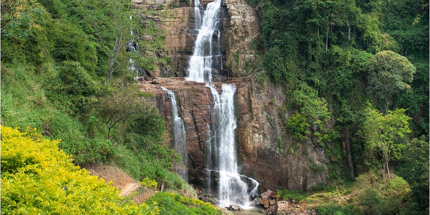 Stunning view of Ramboda Falls, cascading water surrounded by lush greenery and mountains.