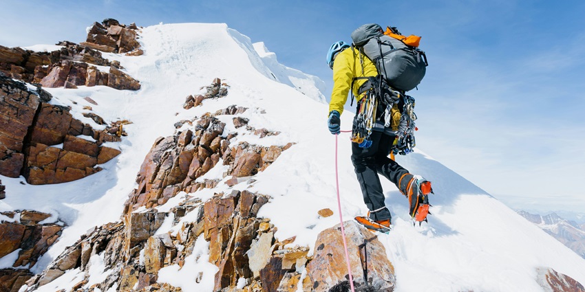 A view of a person rappelling on the snow-capped mountains tied with a rope and harness.