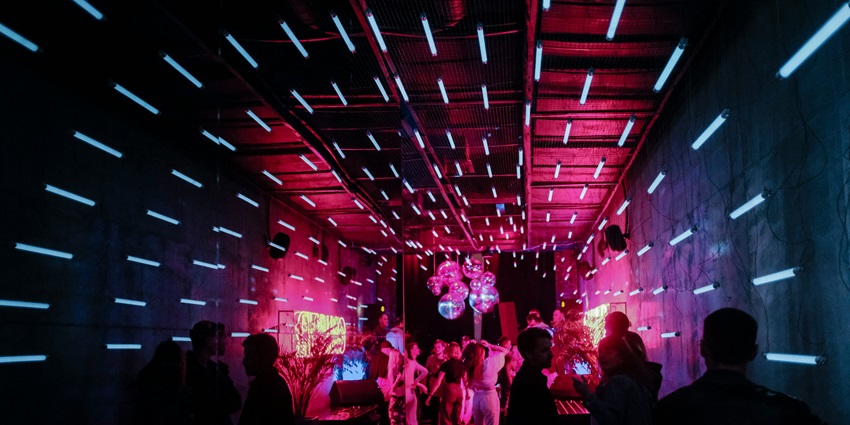 Image of a club where people dancing on the DJ music under colourful disco lights