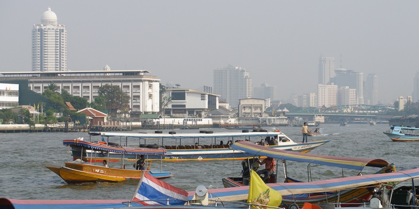 Boats sailing on the Chao Phraya River, with Bangkok's skyline in the background.