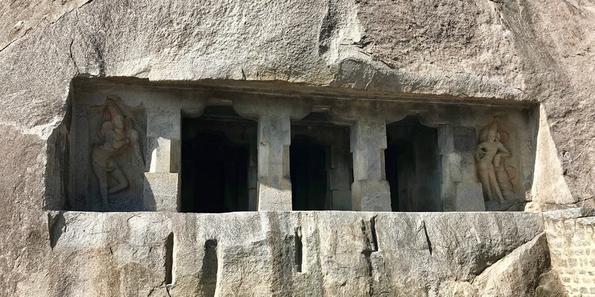 A picture of the entrance of a cave temple with tall pillars carved out of rock