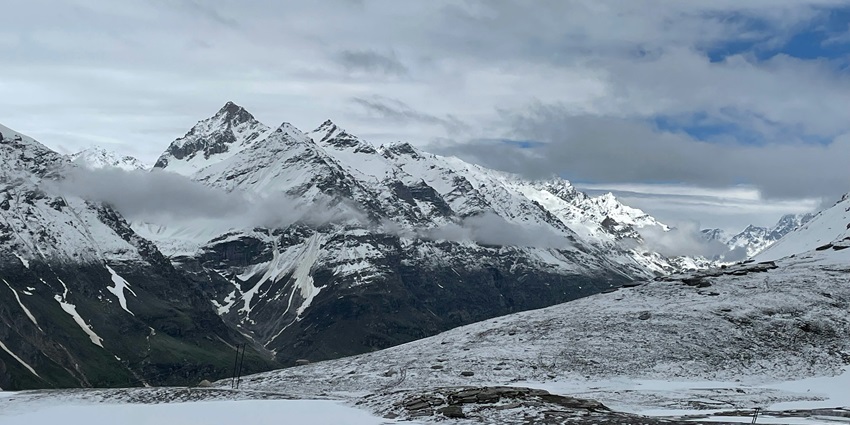 An image of a mountain range covered in snow under a cloudy sky at Rohtang Pass.