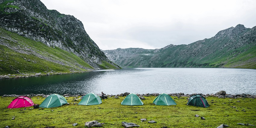 A breathtaking view of a lakeside with colourful tents and mountains in the background.