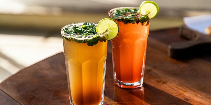 A delicious view of two mocktail glasses kept on a brown table garnished with mint leaves.
