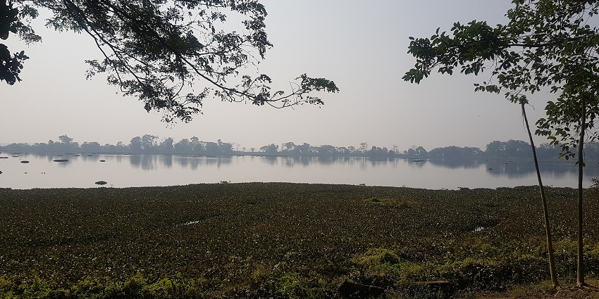 Rudrasagar Tank in Assam with reflective waters surrounded by trees and open sky.