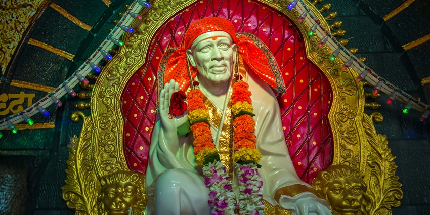 A view of a beautiful statue of Sai Baba adorning a garland and decorated with lights.