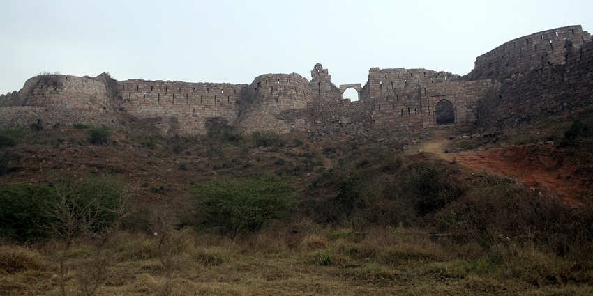 A frontal view of the ruined walls of a historical monument in Silchar, surrounded by bushes