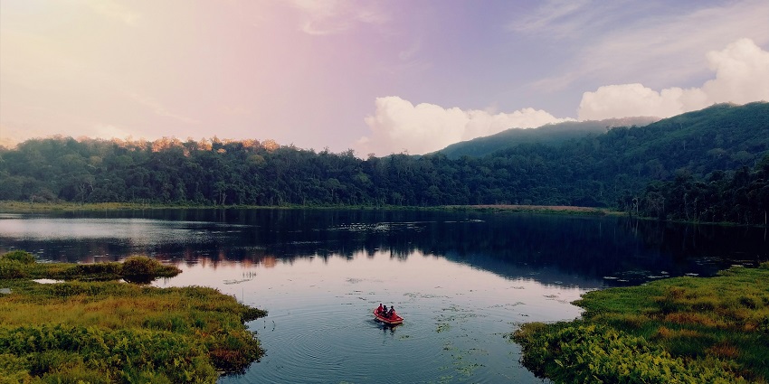 A stunning view of a lake in Mizoram surrounded by lush greenery with a boat on it.