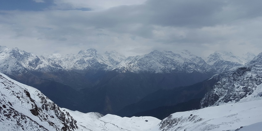 A picture of people moving upwards a mountain covered in snow while trekking in Kasol