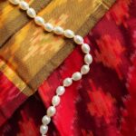 A mesmerising view of a white pearl necklace kept on top of a red and yellow saree.