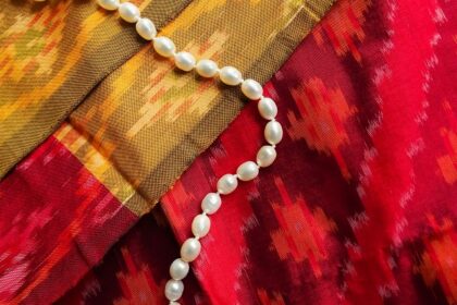 A mesmerising view of a white pearl necklace kept on top of a red and yellow saree.