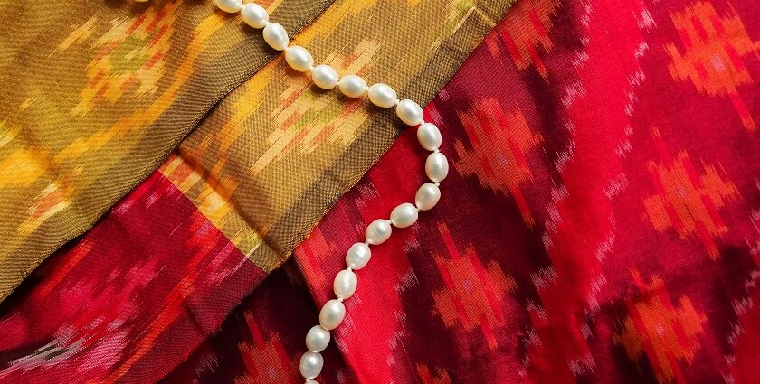 A mesmerising view of a white pearl necklace kept on top of a red and yellow saree.