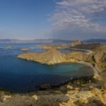 A picture of a hilly, barren-looking island in Indonesia around a sea on a sunny day