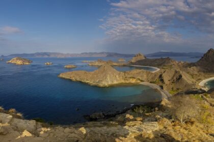 A picture of a hilly, barren-looking island in Indonesia around a sea on a sunny day