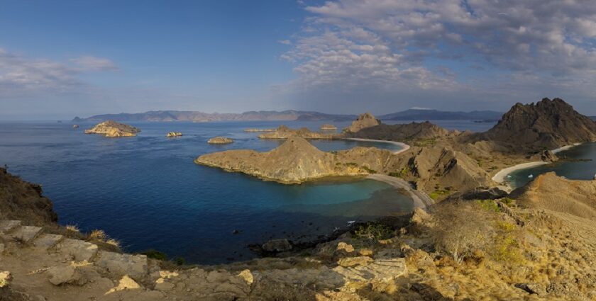 A picture of a hilly, barren-looking island in Indonesia around a sea on a sunny day