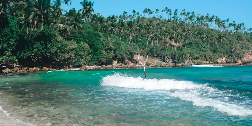 Secluded beach with turquoise water, rocky formations, and lush greenery in Mirissa, Sri Lanka.