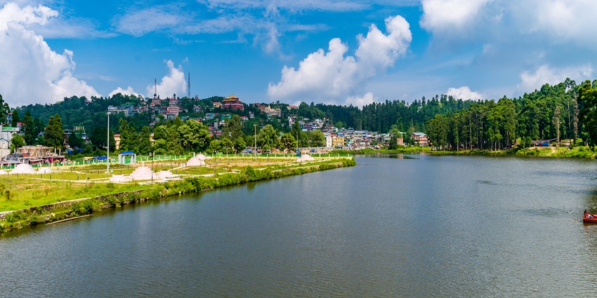 Panorama of Mirik Lake (Sumendu Lake) with surrounding pine trees and distant hills in mist.