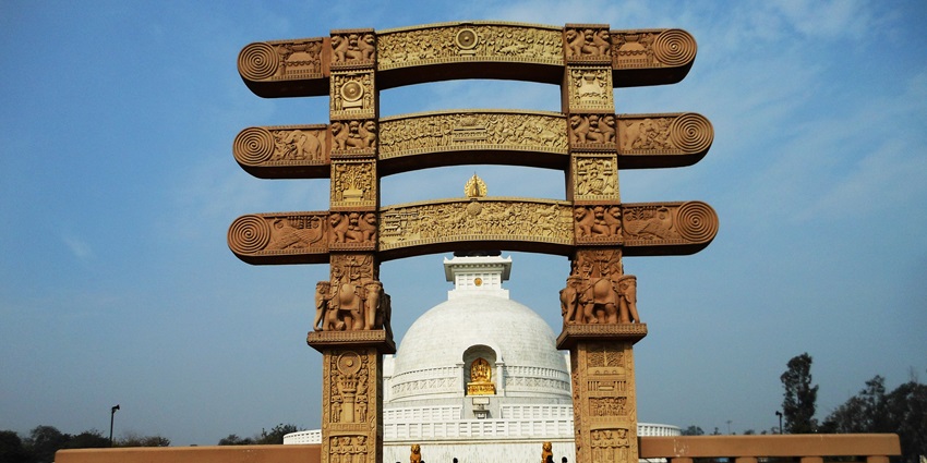 A picture of a Buddhist shrine in Delhi with a tall entry gate in the front having carvings all around