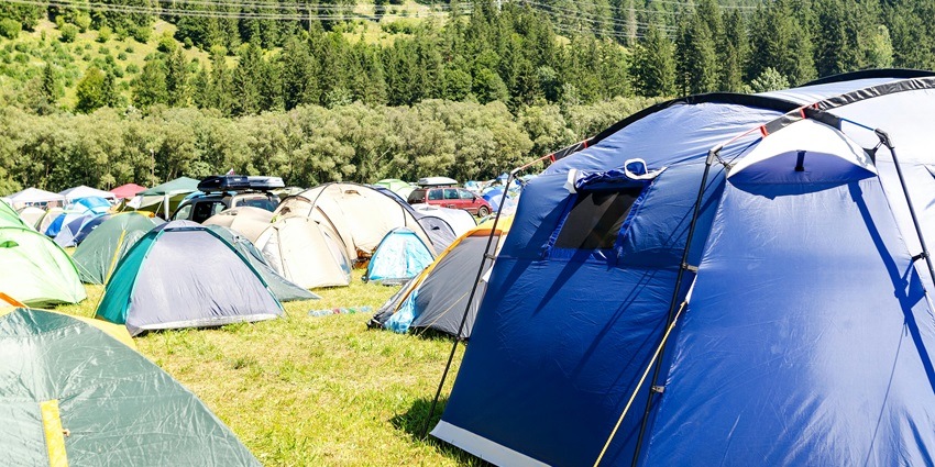 A view of a few camping tents in an open field surrounded by trees during the daytime.