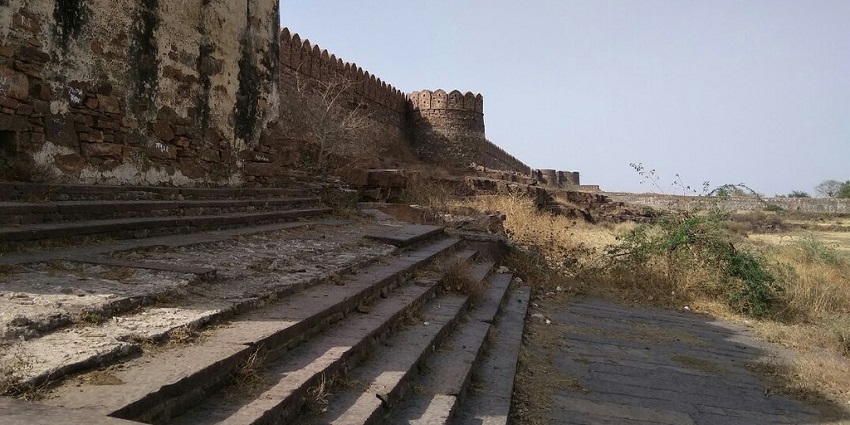 Ruins of Shergarh Fort with crumbling stone walls, arched gateways, and surrounding greenery.