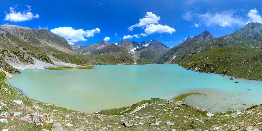 A picture of a majestic lake with turquoise waters, surrounded by lush hills all around