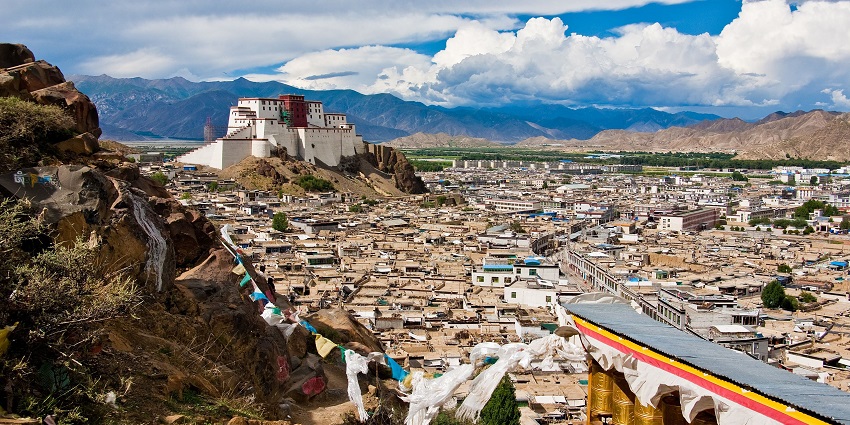View of the city of Shigatse with mountain peaks and a cloudy sky in the background.