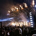 A picture taken at a music festival showing huge crowd and a lit up stage