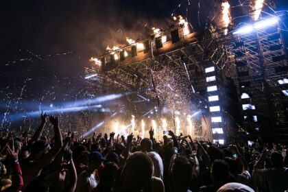 A picture taken at a music festival showing huge crowd and a lit up stage