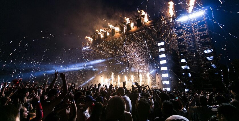 A picture taken at a music festival showing huge crowd and a lit up stage