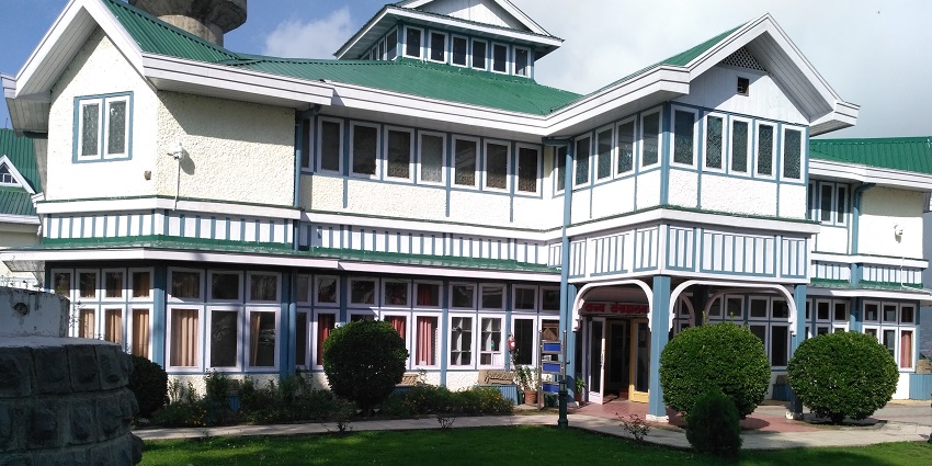 A picture of a white and green building taken from its garden area