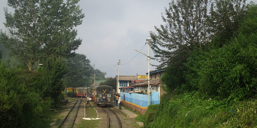 A picturesque view of Shoghi railway station surrounded by lush hills and trees.