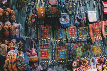 A vibrant view of a shop with colourful crossbody bags and dolls displayed in the front.