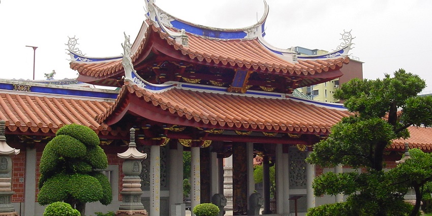 A picture of a temple in Singapore taken from the garden, highlighting the trees and greenery