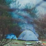 A stunning view of a grey and blue tent amidst a forest with mountains in the background.